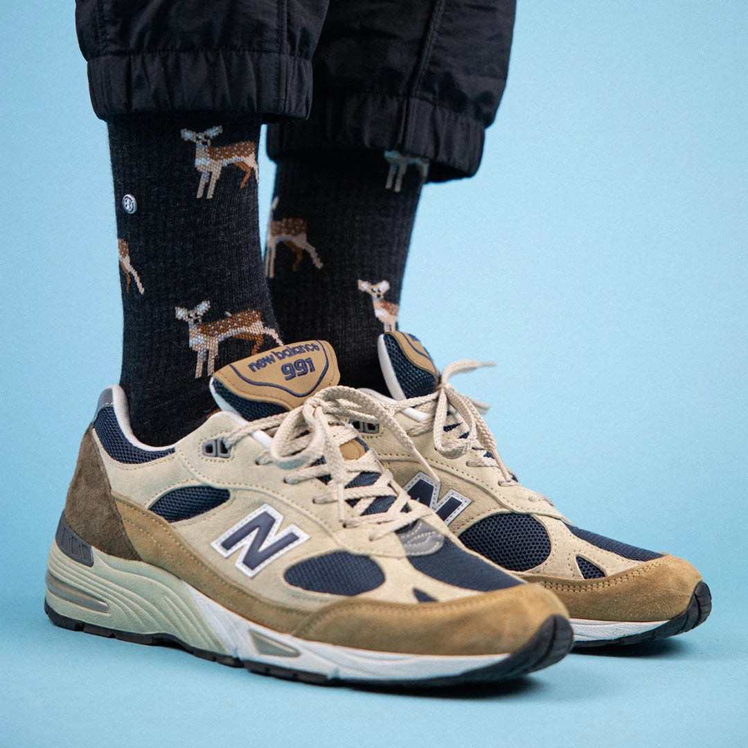 Hirsch Merino Wandersocken mit Frotteesohle, kombiniert mit beigen New Balance Sneakers auf blauem Hintergrund.
