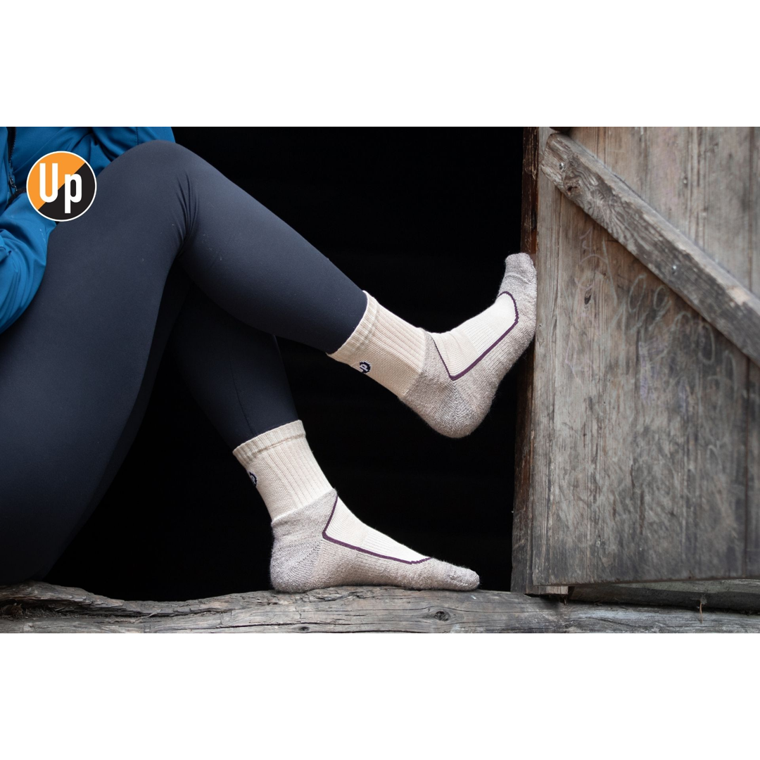 Paar helle Wandersocken mit geripptem Bund und UP-Logo am Knöchel.